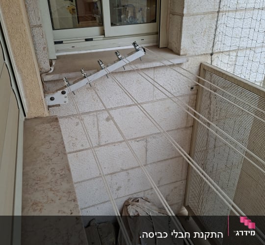 מתקן כביסה מותקן על קיר מרפסת עם חבלים